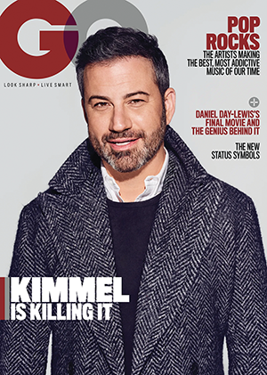 The cover of the GQ magazine featuring Jimmy Kimmel, a white man with dark hair and a salt and pepper beard. He wears a houndstooth coat with the collar turned up, and the headline in the bottom left says "Kimmel Is Killing It"