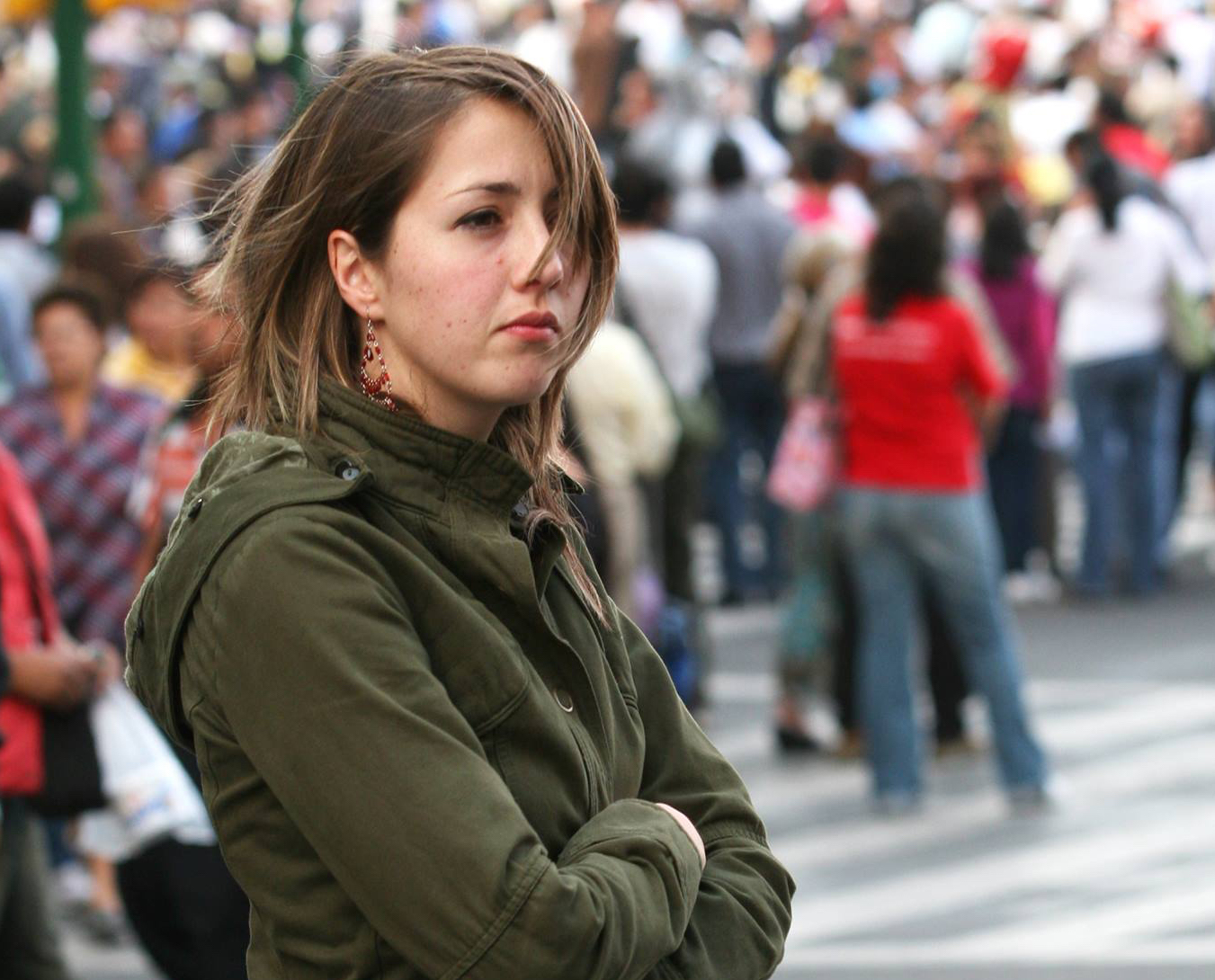 Ana Emilia Felker with brown hair covering half her face wearing an army green jacket with arms folded looking out into a crowd.