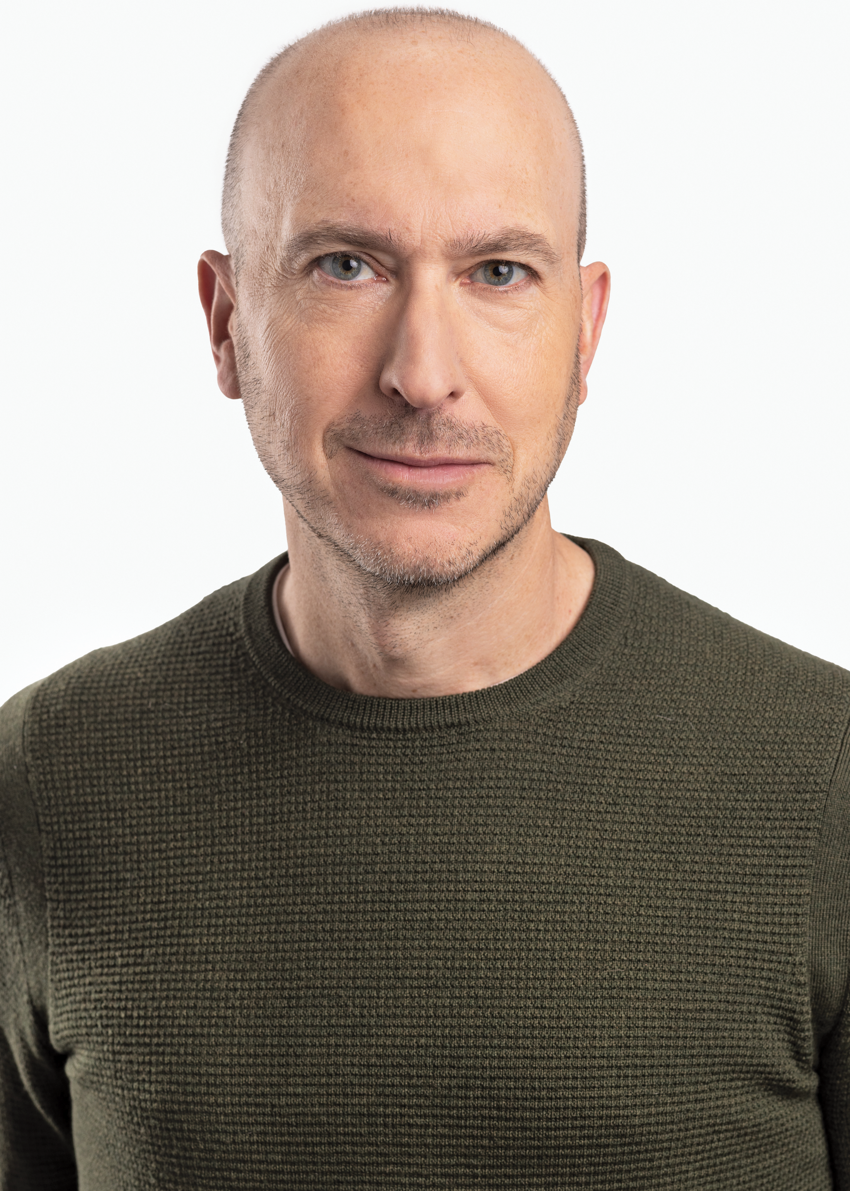 A photo headshot of Aram Fox, a bald white man with light skin and blue eyes. He wears an olive green waffle-knit sweater and is photographed against a white background.