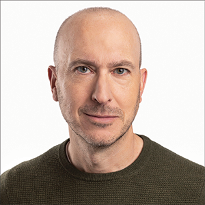 Close-up photo portrait of a man with a shaved head and an olive sweater