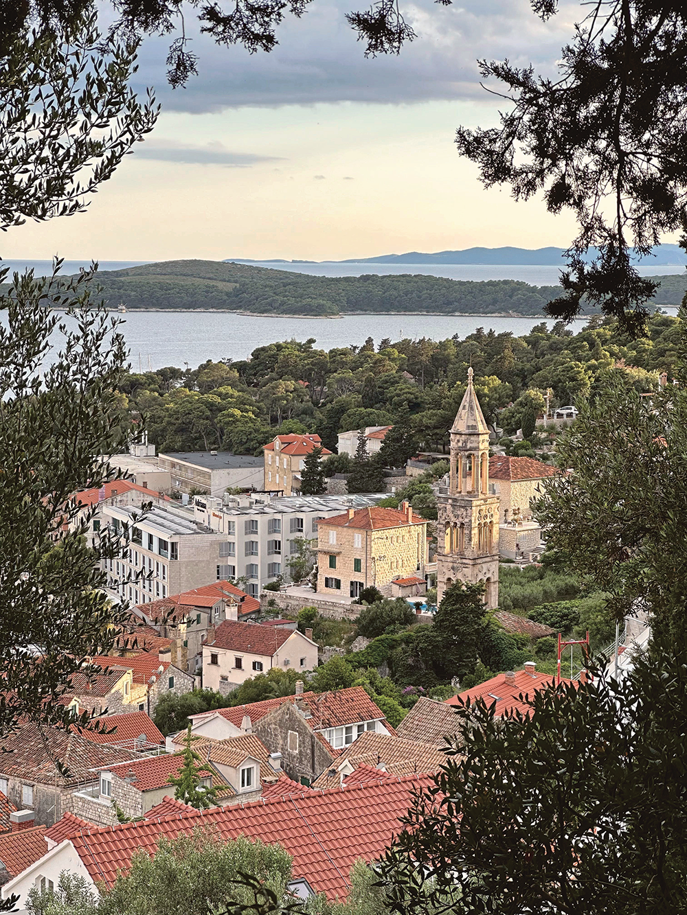 Outdoor photograph of terracotta rooftops, a church, and a bit of the sea from a higher vantage point 