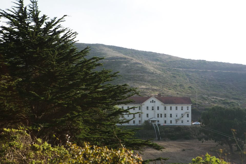 A large white house nestled in trees and mountains.