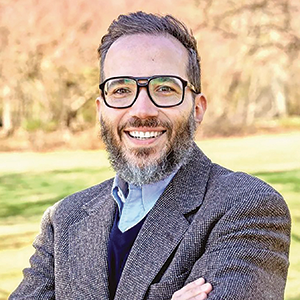 Outdoor photo portrait of a man with short salt-and-pepper hair, a beard, and a tweed jacket