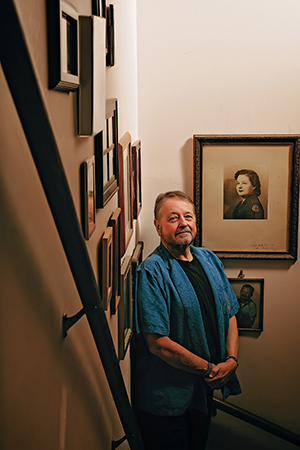 Luis Alberto Urrea stands in the stairway of his home next to a framed portrait of his mother, a member of the Clubmobile service.