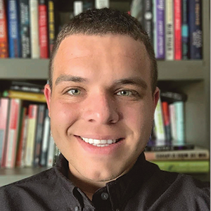 Close-up indoor photo portrait of a young man with short dark hair in front of bookshelves