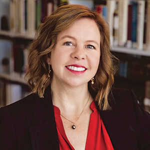 Indoor photo portrait of a woman with chin-length wavy hair and a red blouse in front of bookshelves