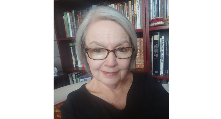 Robin Davidson sits in front of a bookshelf in a black top with glasses and short gray hair.