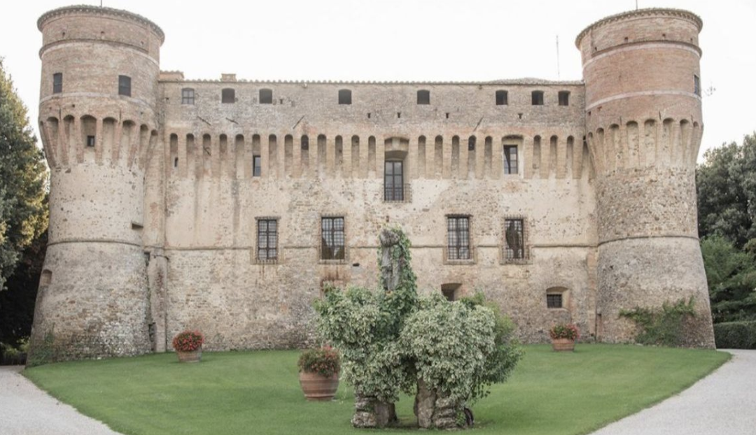 Civitella Ranieri castle, a 15th-century stone building with two round turrets surrounded by green lawn