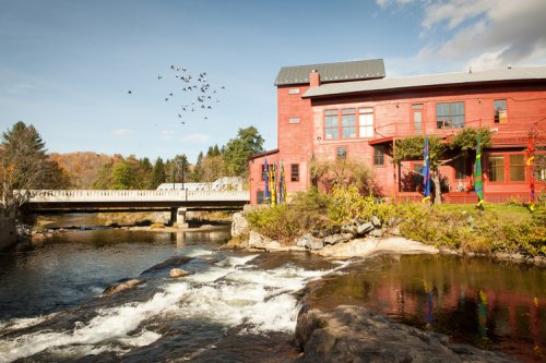 A large red building with a gray roof next to a river.