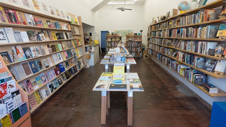 The inside of a bookstore with one long table in the center and bookshelves to the side.
