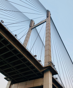 The Time Is Now: Writing Prompts and Exercises A photo of the underside of a tall suspension bridge. Two large pillars point to the sky, each connected to many cables holding up the bridge platform.
