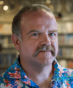Indoor photo portrait of man with gray mustache and colorful shirt