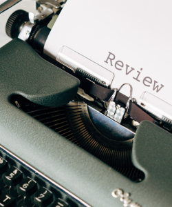 Close-up view of an Olympia typewriter, which holds a single sheet of paper with the word "Review" typed in the center.