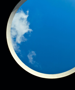 A view of the sky through a large circular opening; wisps of cloud drift at the left edge of the frame.