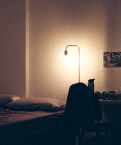 Film photo of a bedroom. A floor lamp illuminates striped pillows on a bedspread, while the rest of the room remains mostly dark.