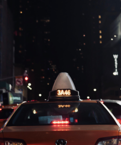 At night in New York City, the backside of a yellow taxicab is illuminated by headlights.