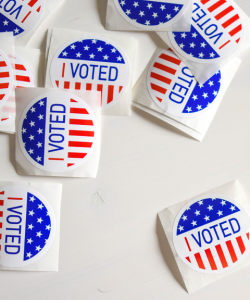 A dozen or so “I VOTED” stickers with an American flag design are spread out on a white table.