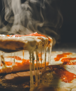A steaming-hot slice of pizza being lifted out of the full pie is trailed by strands of melted cheese.