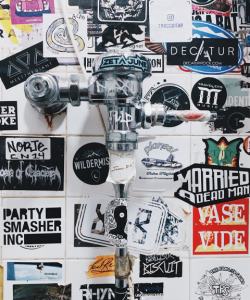 A white-tiled public bathroom wall covered in stickers. A white-tiled public bathroom wall covered in stickers.