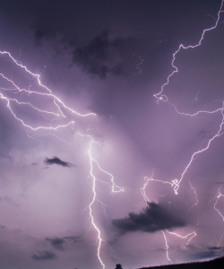 Several bands of lightning crackle above a field; the sky and clouds glow purple. Several bands of lightning crackle above a field; the sky and clouds glow purple.