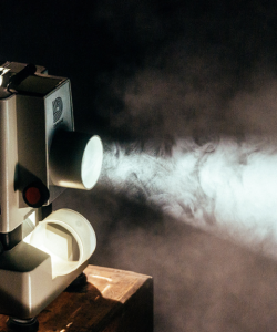 A vintage Dukane film projector shines a beam of light through a dark room