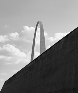 A view of the Gateway Arch in St. Louis. The top half of the stainless steel monument is visible, while the bottom half is obscured by a large wall.