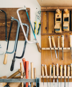 Inside a woodworker's studio, saws, files, mallets, and hammers are stored in various wall units.