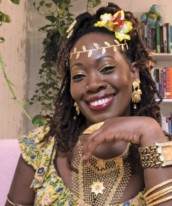 Literary MagNet: Camille U. Adams Camille U. Adams, a dark-skinned Black Trinidadian woman bedecked with gold jewelry and gold makeup. She smiles brightly and poses with one hand in front of her face.