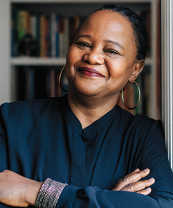 Indoor photo portrait of a woman smiling, with her arms crossed, in front of bookshelves