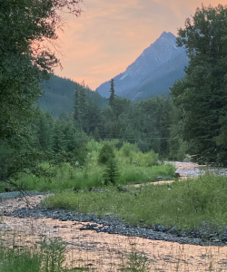Scenic photograph of distant mountains, a river winding through greenery in the foreground, and a cloudy orange sky