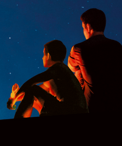 Close-up of the cover of Richard Powers’s Bewilderment. A child and an adult sit next to each other gazing up at the night sky. They are partially illuminated by a warm orange light that casts them in dramatic shadows.