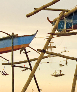 Close-up of the cover of Patrick Rosal’s The Last Thing. Toy-sized wooden boats hang suspended from scaffolding that holds larger wooden boats. The sky in the background is a soft yellow.