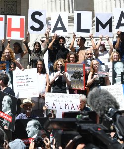 A crowd of people holding signs that say "Stand with Salman" stand on the steps of an imposing building.