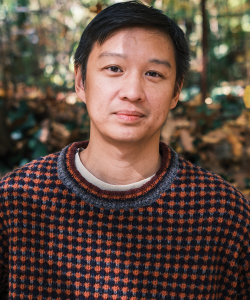 Constancy and Surprise: What Editing Magazines Taught Me About Writing Fiction A high-quality photo portrait of Kevin Nguyen, a young Asian man with tan skin and short black hair parted to the right side. He wears a fuzzy checkered sweater in orange and black, and stands in a forest with a neutral expression.