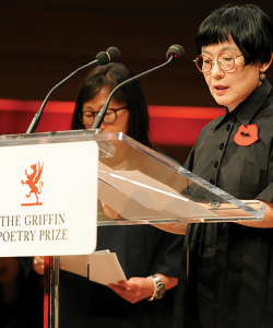 South Korean poet Kim Hyesoon reading at a clear podium with the Griffin Poetry Prize logo, with translator Don Mee Choi behind and on the left.