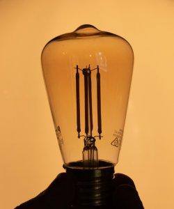 An old-fashioned lightbulb is held up against a warm orange-y background by a silhouetted hand.