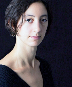 A woman with short grown hair, gold earrings and a black shirt. Lily Meyer