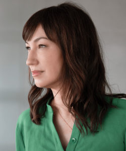 Marie Mutsuki Mockett Indoor photograph of woman with long dark hair and bright green shirt facing off to her right side
