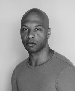 A black and white portrait of poet Nicholas Goodly wearing a long-sleeved t-shirt.