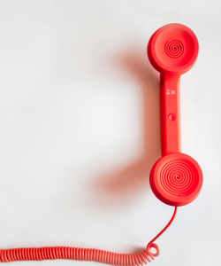 A coral-colored telephone handset on a white background. The cord stretches offscreen.
