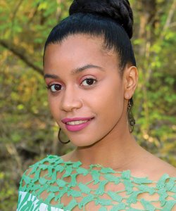 Jennifer Maritza McCauley, a woman with brown skin and dark hair pulled up into a bun, smiles at a three-quarters angle to the reader. She wears a green shirt.