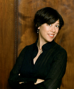 Susan Choi Photo portrait of a woman with short dark hair and dark blouse leaning against a wall