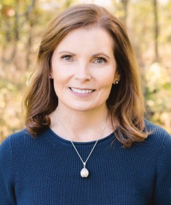 Outdoor photo portrait of a woman with shoulder-length reddish hair, wearing a dark blue top and chain with a charm around her neck