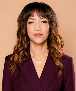 A woman with long light brown hair in front of a pale pink background. Tiana Clark