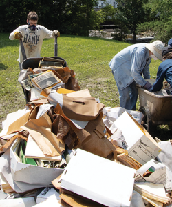 Six volunteers work together to remove debris in a field of grass. The debris mainly consists of paper and cardboard boxes.
