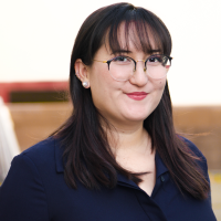 A head shot of Amanda Orozco, a person with dark hair and glasses wearing pearl earrings and a blue shirt