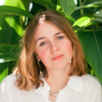Headshot of Eleanor Cousins Brown, seated outside in front of dense green plants