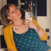 Headshot of Krista Cox, who leans playfully as she takes a picture of herself in a mirror
