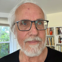 Headshot of Askold Melnyczuk, who wears glasses as he appears before a window with greenery behind it