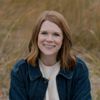 Headshot of Samantha Shea, seated outside in front of a field of brown reeds
